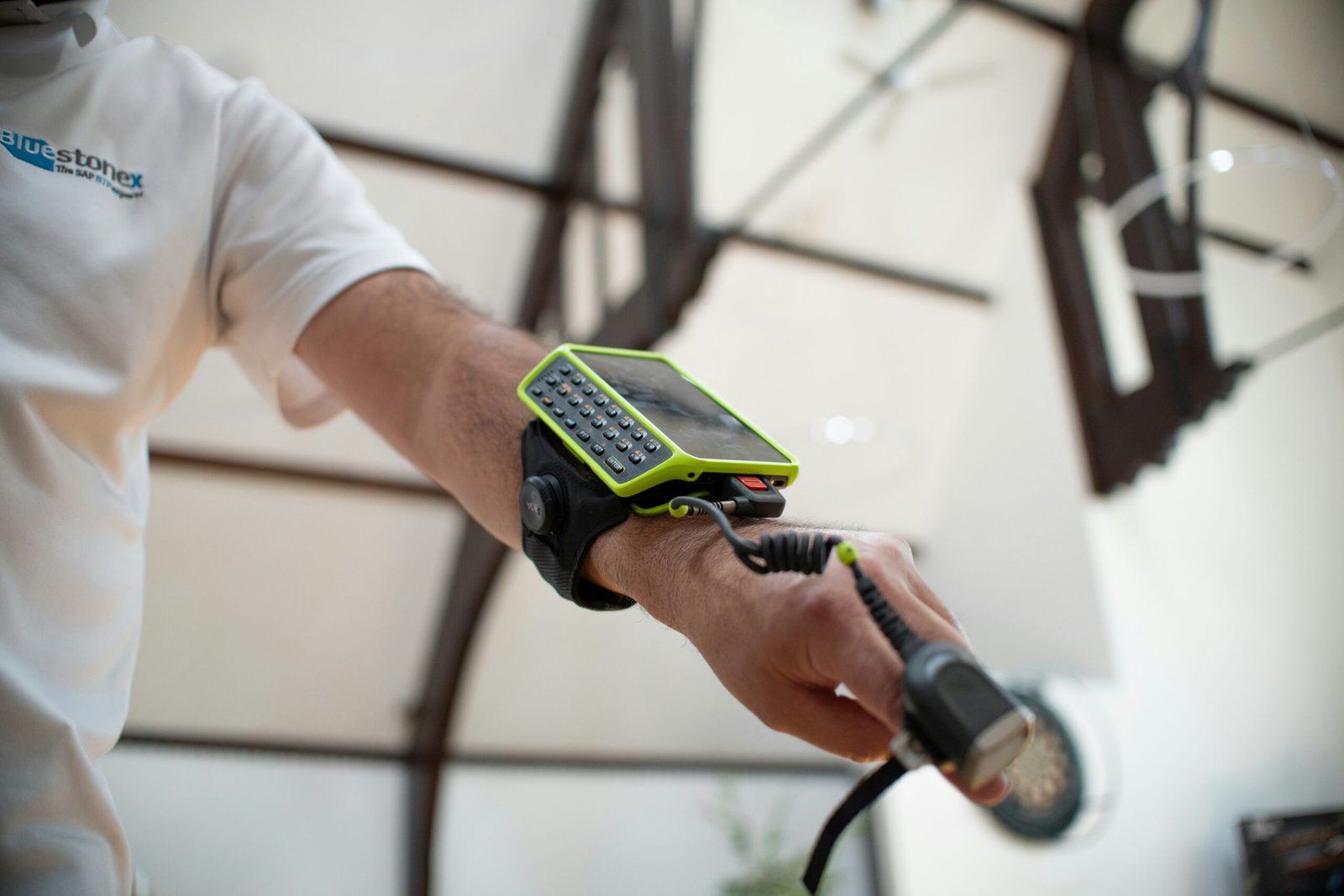 Close-up of a warehouse worker wearing a Bluestonex branded shirt, using a wrist-mounted lime green mobile computer and a finger-mounted ring scanner.